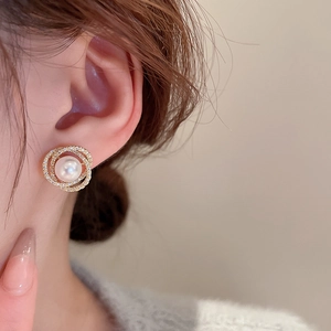 Détail de boucles d'oreilles perles dorées avec zircon portées dans un style rétro