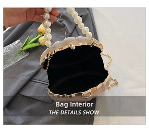 Detail view of shell bag with pearl handle and golden chain on a grey blazer
