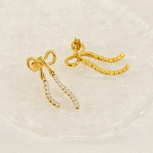 Elegant gold bow earrings with crystal tassels on a textured glass display plate