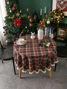 Detailed view of round red tartan tablecloth with fringe in a cozy Christmas setting