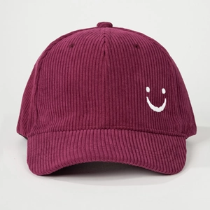Detailed texture of burgundy corduroy baseball cap with white embroidered smiley face
