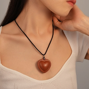 Close-up of vintage brown faux leather heart pendant with woven edge on black cord