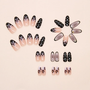 Detail of almond-shaped press-on nails featuring black floral, polka dot, and gold bead accents
