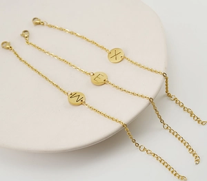 Detailed view of three 18K gold-plated steel bracelets with W, E, and X alphabet charms