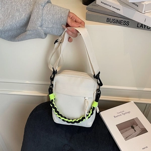Detail of off-white canvas messenger bag featuring vibrant neon green woven chain ornament