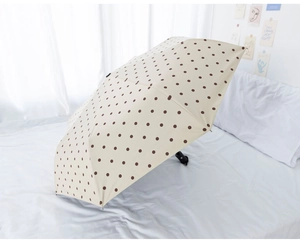 Detail of cream folding umbrella with brown polka dots on a minimalist white background