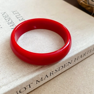 Macro shot of a vibrant red resin bangle with a polished finish placed on an art book