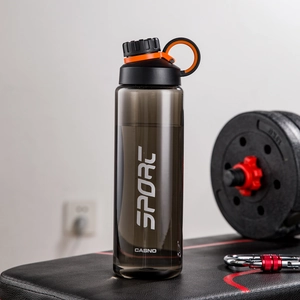 Close-up of black plastic sport water bottle with carry strap in a gym setting