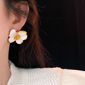 Close-up of vintage flower earrings with white enamel petals and gold edges worn by a model