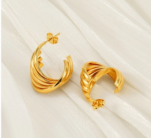 Gros plan de boucles d'oreilles torsadées dorées 18 carats sur fond de tissu en soie blanche