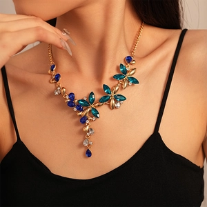 Macro shot of gold necklace featuring blue and emerald green crystals in flower pendant