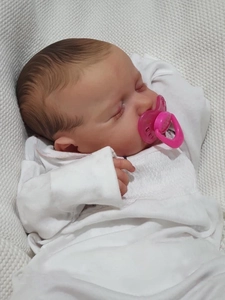 Close-up of a sleeping 19-inch reborn baby doll with brown hair and pink pacifier