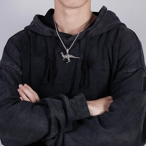Close-up of a silver dinosaur pendant on a rope chain worn with a black hoodie
