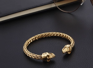 Macro detail of golden skull cuff bracelet with braided design on dark leather background
