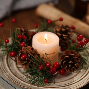 White pillar candle with pine cones and red berries wreath on ceramic plate