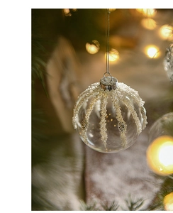 Close-up of clear glass Christmas ball with white pearls and gold sequins on a tree