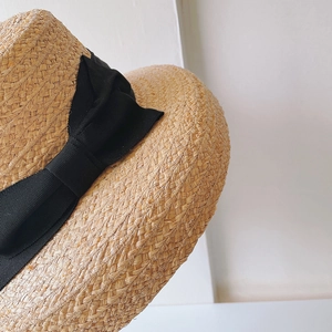 Close-up of natural raffia straw sun hat texture with a wide black grosgrain bow detail