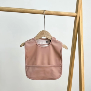 Detail of baby waterproof bib in dusty rose with large food catcher on wooden hanger