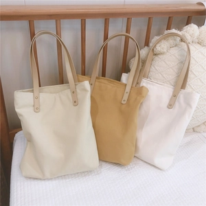 Three canvas tote bags in white and yellow shown on a bed for a minimalist aesthetic