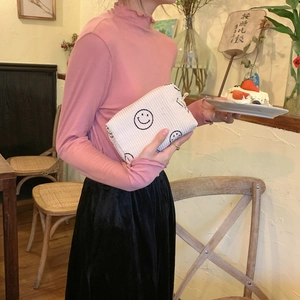 Detail of white corduroy makeup bag with black embroidered smiles held by a model