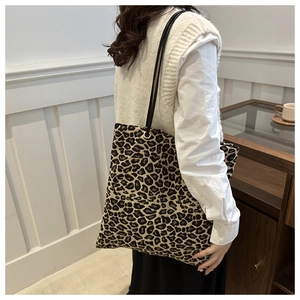 Detail of leopard print tote bag featuring black leather straps and gold metal ring hardware