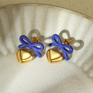 Detail of blue ribbon bow earrings with 18K gold heart charms on white ceramic plate