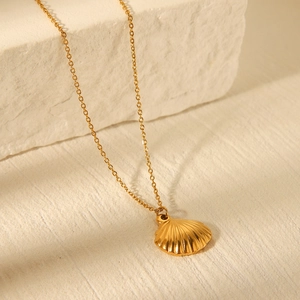 Close-up of golden seashell pendant necklace on textured white stone with warm lighting