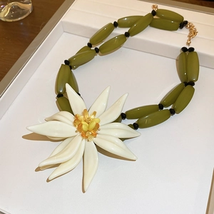 Macro view of a large white 3D resin flower necklace with olive green beads detail