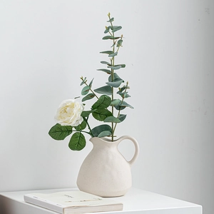 Matte beige ceramic teapot vase with white roses and eucalyptus leaves for table decor