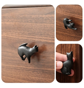 Close-up of matte black cast iron cat-shaped handles on a dark walnut wood cabinet