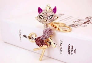Close-up of golden cat keychain with purple and clear rhinestones on a white book