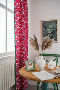 Detail view of cotton linen curtain with red floral patterns and green fringe tassels