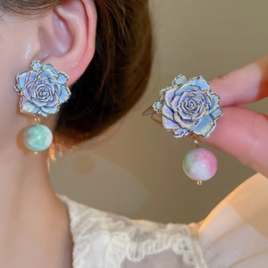 Detailed close-up of a blue rose earring with gold edges and marbled glass beads