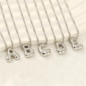 Polished silver bubble initial necklaces with A-E letter pendants on a textured surface