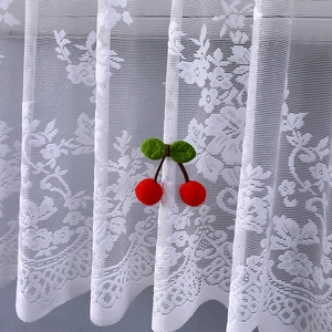 Detail of white lace cabinet curtain with red cherry pom-pom tassels and floral pattern