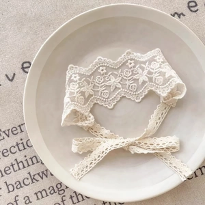 Détail du bandeau en dentelle crème avec broderie florale et ruban sur plateau céramique