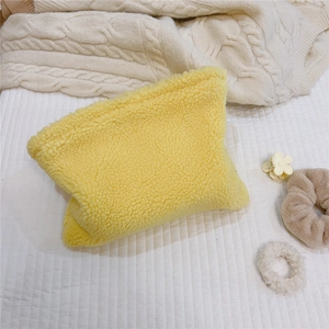 Detail of yellow sherpa fleece makeup bag on a cozy knitted blanket with hair accessories