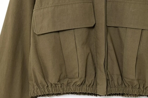 Close-up of olive green utility jacket featuring large flap pockets and elastic hem details