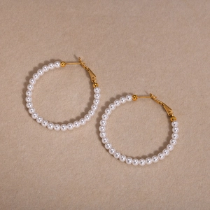 Detail shot of elegant C-shaped gold hoops featuring white round pearls on beige velvet