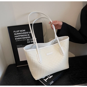 Detail shot of a white woven tote bag with dual handles shown in a stylish studio setting
