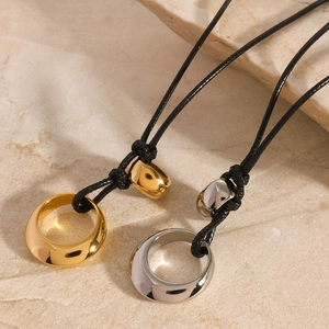 Detail of gold and silver ring pendants on adjustable black cords over beige stone