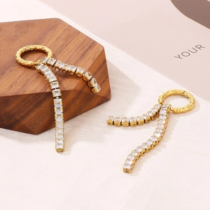 Detailed close-up of golden tassel earrings with clear square zircons on wooden props