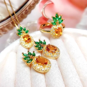 Detailed close-up of pineapple jewelry set with orange and green gems in a pink box
