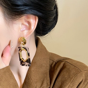 Detail view of retro leopard print resin earrings worn by a model in a brown blazer