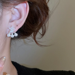 Dettaglio di orecchini con stella in zircone e tripla perla indossati da una modella