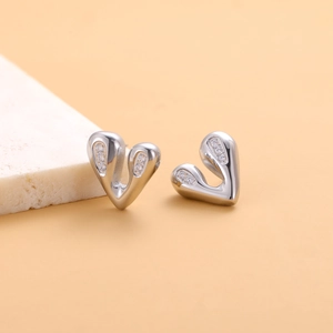 Macro shot of silver heart earrings featuring zircon stones on a warm orange backdrop