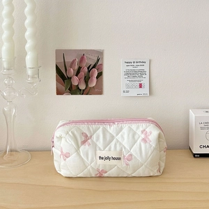 Detail of white quilted floral makeup bag with pink zipper and woven house brand label
