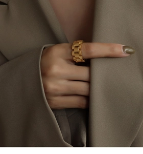 Detailed view of a gold chain ring with a watch-strap design on a brown fabric background