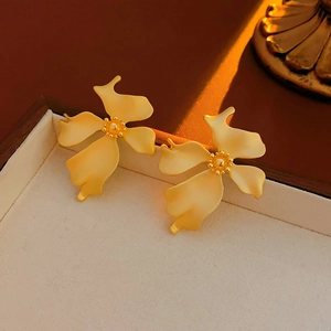 Detailed macro of gold flower stud earrings with matte texture in a wooden jewelry box