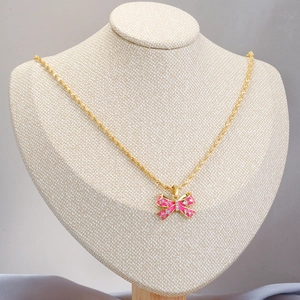 Golden necklace with pink enamel bow pendant and white zircon inlay on mannequin